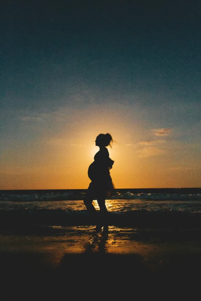 Silhouette d'une femme enceinte sur la plage au coucher du soleil